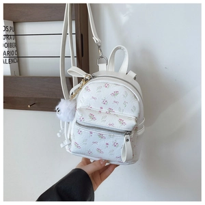 Vue détaillée du mini sac à dos blanc avec motifs floraux et pompon en peluche