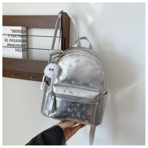 Sac à dos floral argenté à texture métallique avec pompon blanc sur fond en bois