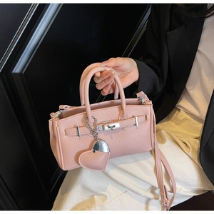 Close-up of pink pebbled leather handbag featuring silver hardware lock and heart charm