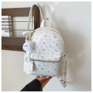 Détail d'un mini sac à dos en cuir PU blanc avec motifs floraux et pompon en peluche