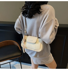 Detail of cream-colored PU leather crossbody bag featuring a pink woven decorative charm