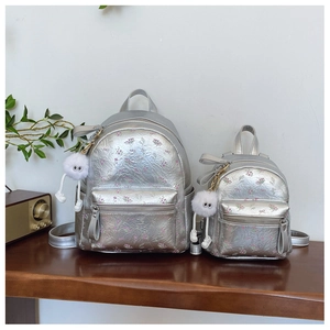 Détail de deux sacs à dos argentés à fleurs avec porte-clés en peluche sur table