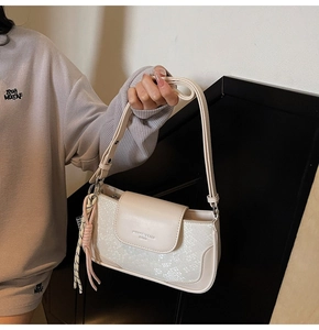 Close-up of minimalist cream baguette bag with snakeskin texture and pink charm detail