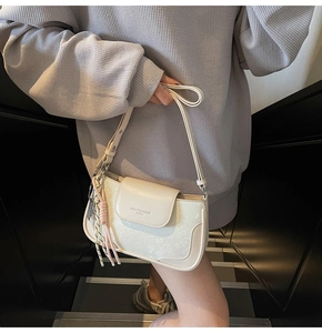 Detail of cream white faux leather shoulder bag with magnetic clasp and woven tassel accessory