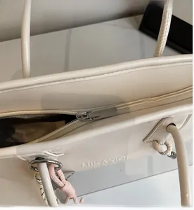 Detail of a cream leather handbag featuring a smooth silver zipper and embossed logo