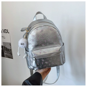 Détail du sac à dos argenté métallisé avec motifs floraux et accessoire en peluche