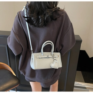 Detail shot of light grey lychee leather handbag worn by model for size reference