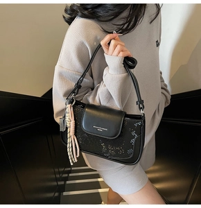 Detail of black textured crossbody bag featuring smooth flap with brand logo and tassel