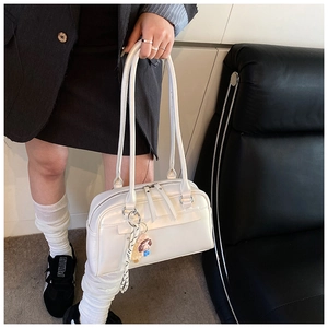 Detail einer weißen Leder-Boston-Tasche mit Doppelreißverschluss und Puppenanhänger