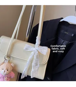 Close-up of cream underarm bag featuring delicate lace bow and plush bear charm detail