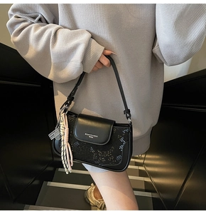 Close-up of black animal texture shoulder bag with woven fringe and metal charm details