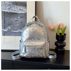 Détail du sac à dos argenté métallisé avec motif floral et nœud décoratif sur le dessus