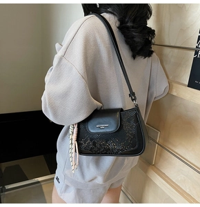 Detail of black leather underarm bag with snake pattern and woven rope accessory