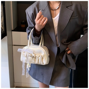 Detail of cream white pleated bowling bag with lace bow and pearl charm decoration