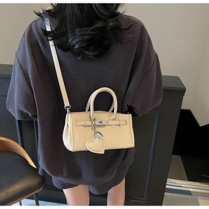 Detail view of cream leather handbag with heart charm and classic metal lock