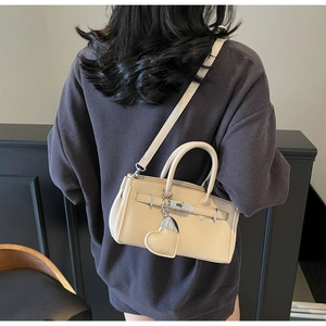 Detail of beige lychee leather mini crossbody bag featuring a silver heart charm and lock