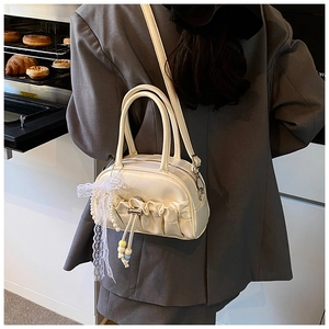 Detail of a pleated bowling bag with cream lace ribbons and pearl charms in a cozy cafe