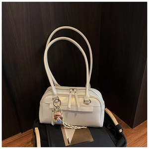 Detail einer weißen Handtasche mit rundem Griff und süßem Anhänger auf Holztisch