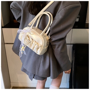 Close-up of pleated cream handbag with lace bows and pearl charms worn as a crossbody bag