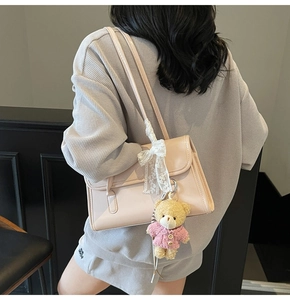 Detail of a chic cream-white shoulder bag featuring a cute teddy bear and lace bow charm