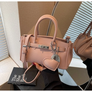 Close-up of pink lychee grain leather handbag with gold lock and heart charm