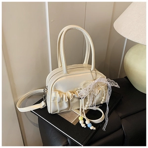 Detail of cream pleated bowling bag with pearl beads and lace bow on a book