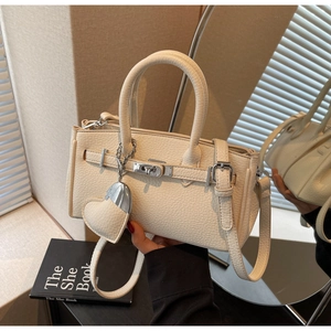 Detail of beige lychee texture leather handbag with silver turn-lock and heart pendant