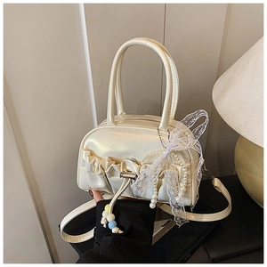 Detail of cream pleated bowling bag with pearl charms, lace bows, and glossy finish