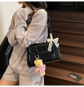 Close-up of black glossy shoulder bag with lace bow decoration and cute bear pendant detail