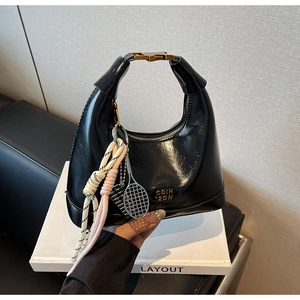 Detail of black glossy leather hobo bag with gold hardware and tennis racket charm