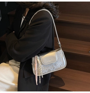 Close-up of silver snakeskin crossbody bag with woven pendant on model's shoulder