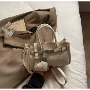 Detail of cream lychee texture crossbody bag with classic metal lock and heart charm