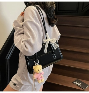 Detail of black patent leather shoulder bag with lace bow and cute teddy bear charm
