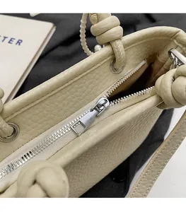Detail of silver smooth zipper and textured lychee leather on cream bucket bag