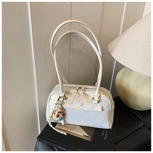 Detail der weißen Lederschultertasche mit Cartoon-Anhänger auf einem Buchhintergrund