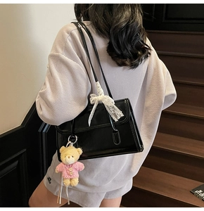 Detail view of black patent leather shoulder bag with lace bow and plush bear charm