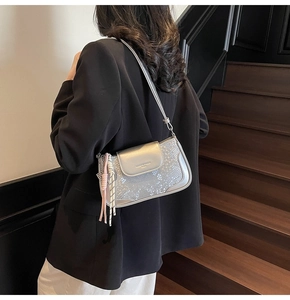 Silver snakeskin textured shoulder bag with woven tassel shown on a stylish model