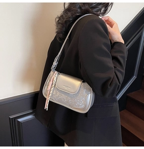 Detail view of silver crossbody bag with scale texture and pink woven tassel charm