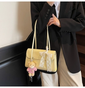 Close-up of cream underarm bag with white lace bow and pink teddy bear pendant detail