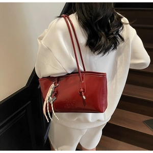 Détail d'un sac à bandoulière rouge foncé brillant avec poignée nouée et breloque