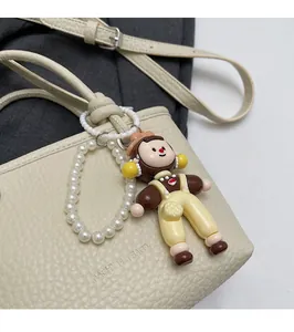 Detail of cute cartoon doll pendant with pearl chain on white textured leather bucket bag