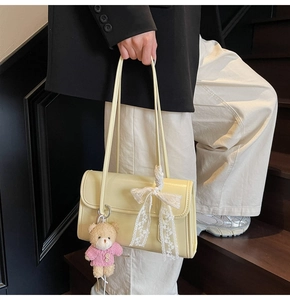 Detail of light yellow shoulder bag with white lace bow and brown plush bear charm