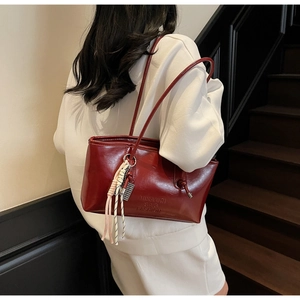 Détail d'un sac sous le bras en cuir verni bordeaux avec bandoulière nouée et pompon