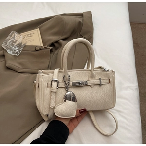 Detail of creamy white litchi grain leather bag with metal lock and heart pendant