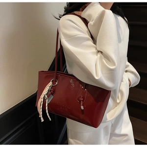 Gros plan du sac fourre-tout en cuir verni bordeaux avec poignée nouée et pompon