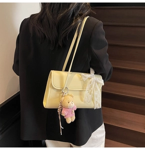 Detail of a yellow glossy shoulder bag with a lace bow and a cute teddy bear pendant