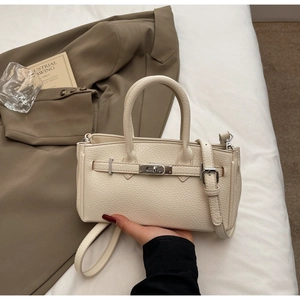 Close-up of lychee textured cream leather handbag with classic metal lock and top handle