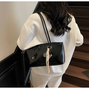 Détail d'un sac cabas noir brillant avec lettres embossées et pendentif raquette