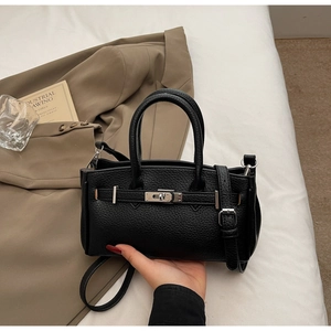 Detail of black litchi grain leather handbag with silver lock and detachable strap