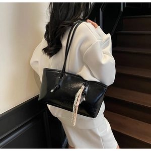 Détail d'un sac cabas noir brillant avec poignées nouées et un charme tissé décoratif